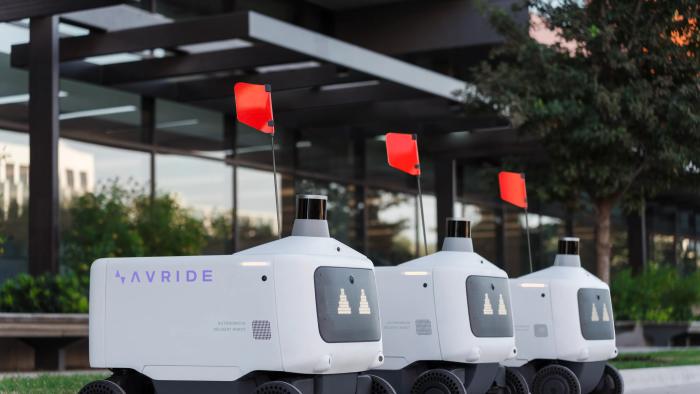 Three Avride autonomous delivery vehicles parked in a line. They have red flags.