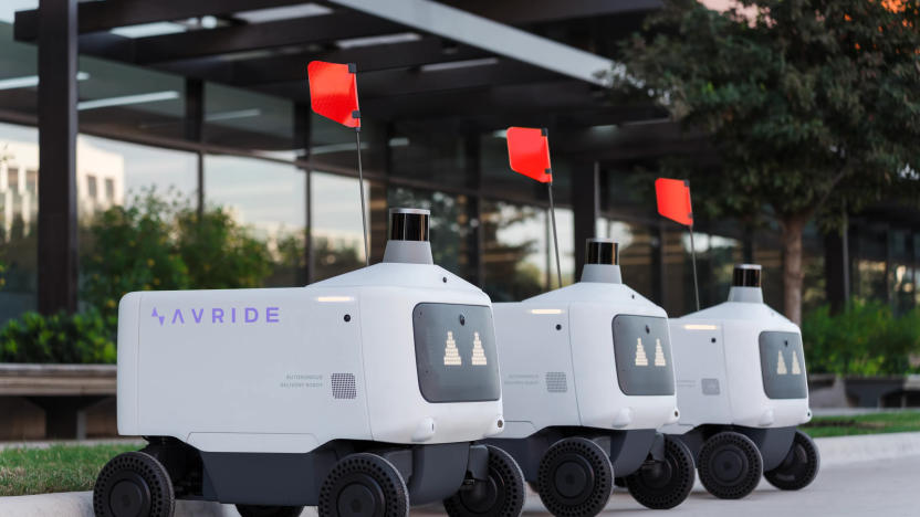 Three Avride autonomous delivery vehicles parked in a line. They have red flags.