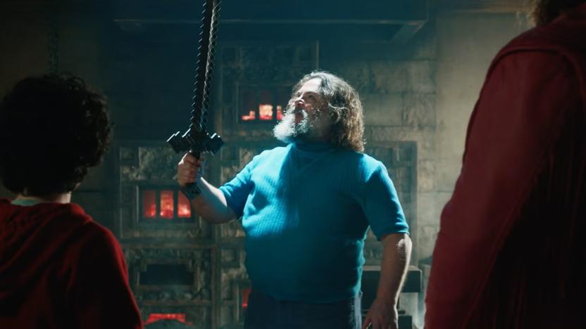 A still from A Minecraft Movie showing Jack Black wearing a blue shirt as the iconic character Steve, holding a crafted sword. We see two other characters from the back, both wearing red and looking at Jack Black